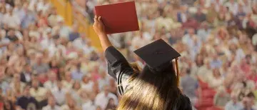 Student crossing stage at graduation, holding up diploma