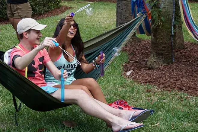 Two students sit in hammock, blowing bubbles. 