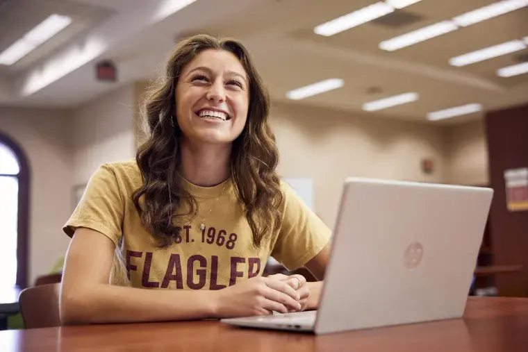 A Flagler College student smiles as she works on a laptop.