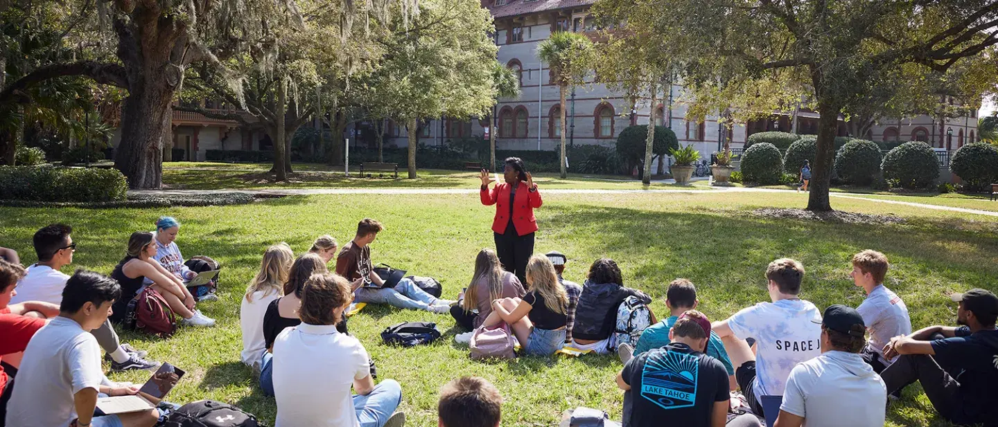 A professor teaching to their class of students who are sitting on the grass of the West Lawn