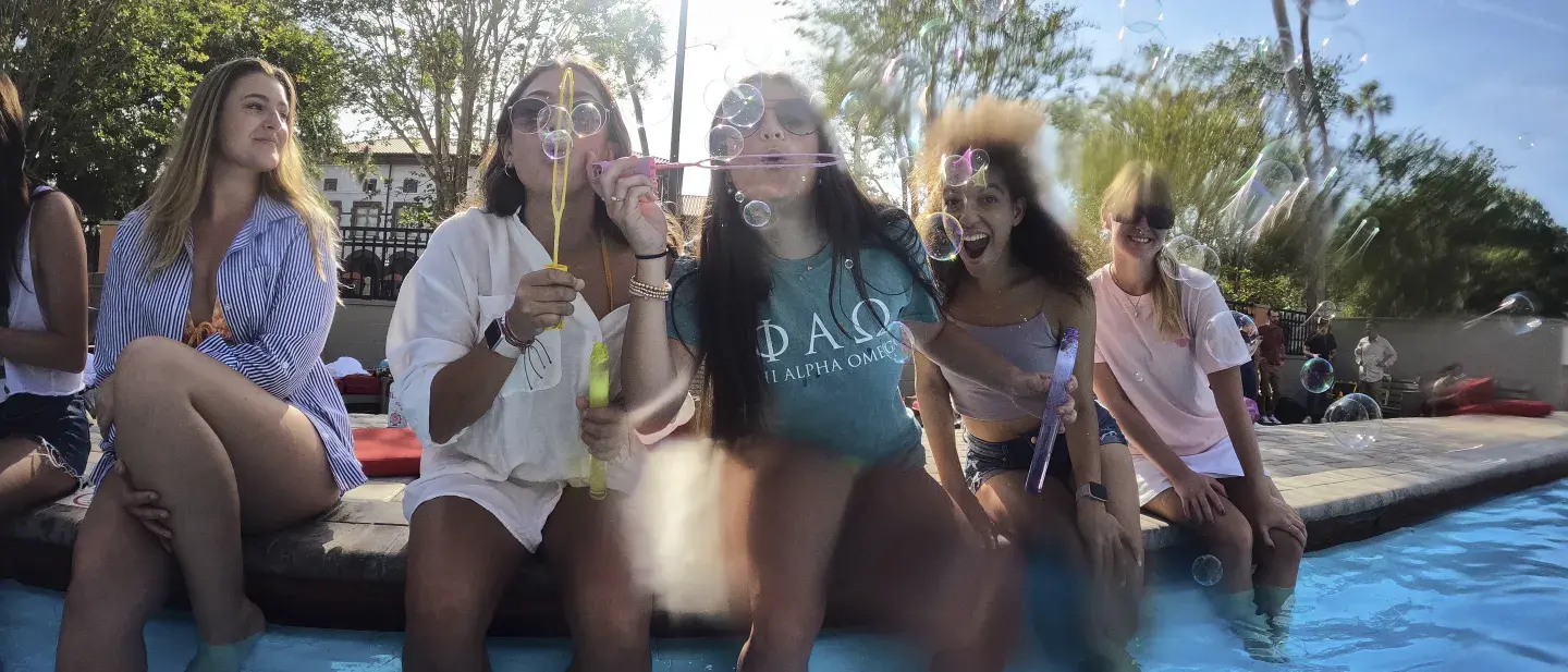 Students sitting pool-side, blowing soap bubbles over the water