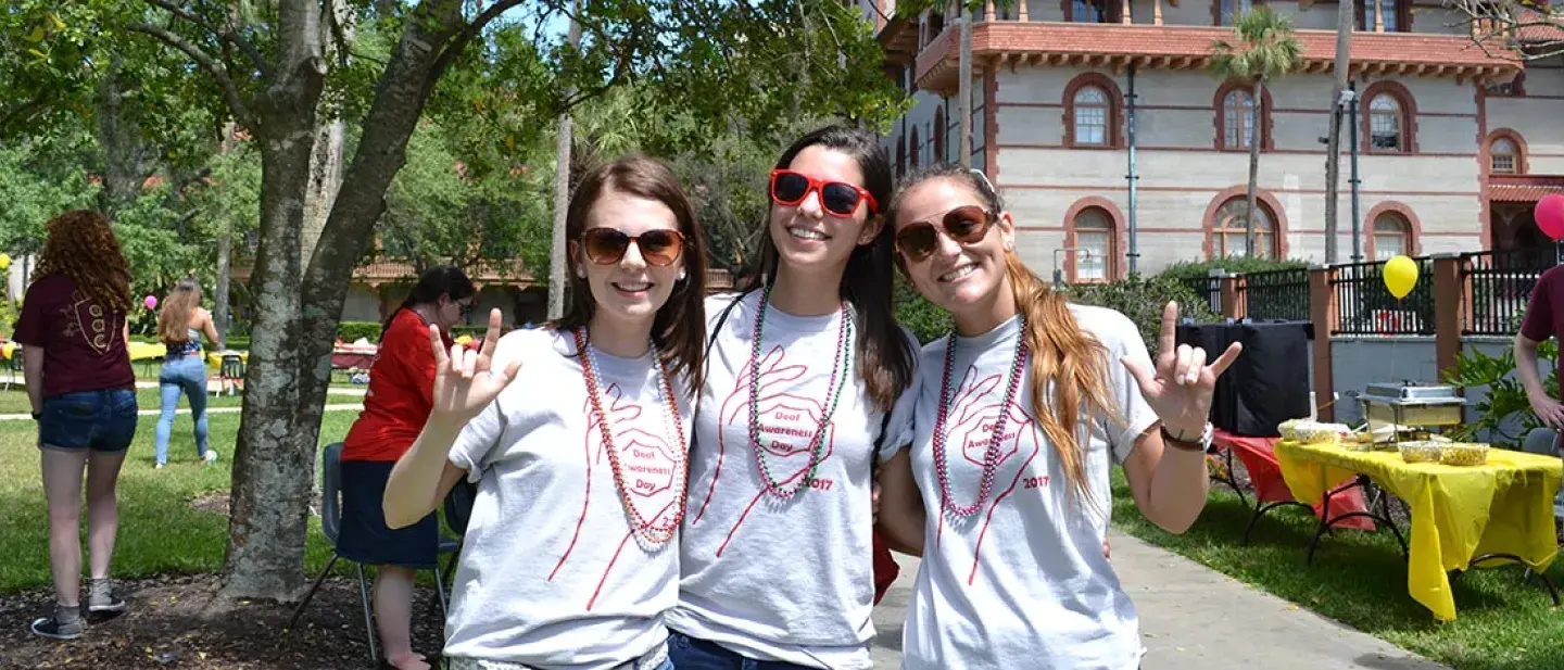 Three students sign "I love you" wearing t-shirts for Deaf Awareness Day. 