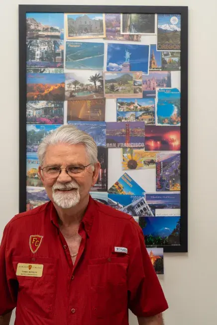 Bennett standing in front of framed postcards in current office