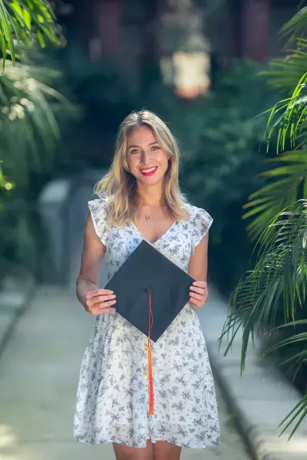 Lindsey Wood holding her cap and standing on a path with trees on either side