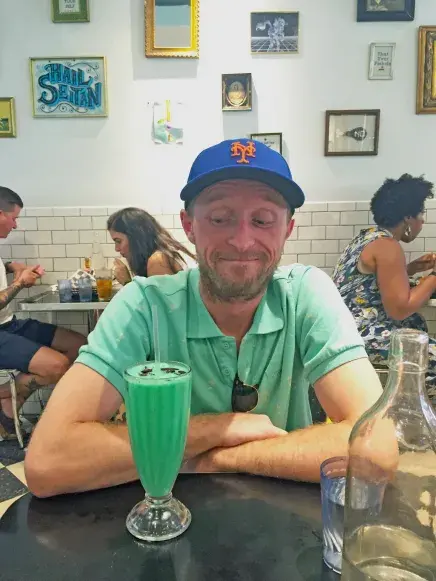 Ryan Brower in NYC cafe with Mets hat on and diner milkshake
