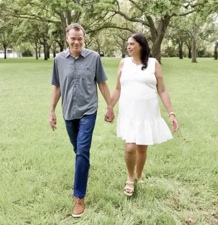 Lulu and Dave Benedict walk through a wooded area while holding hands
