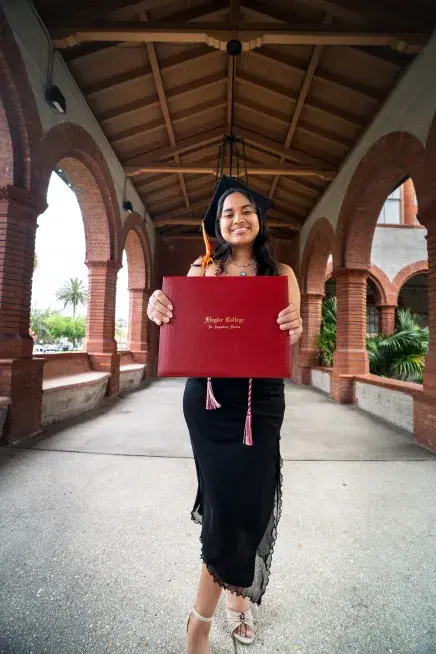 Julia Hewitt stands holding her diploma out towards the camera
