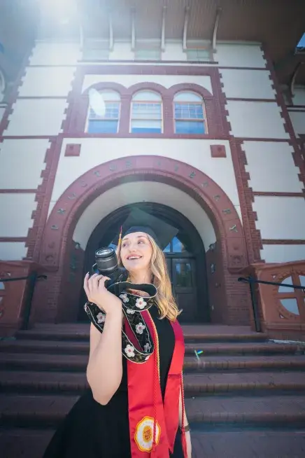 Zoey Nettles holds a camera in front of Proctor Library
