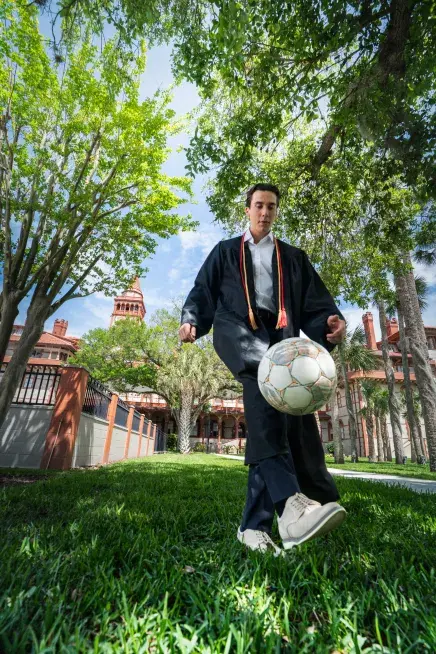 Jesse Van Krimpen juggling a soccer ball in his graduation gown