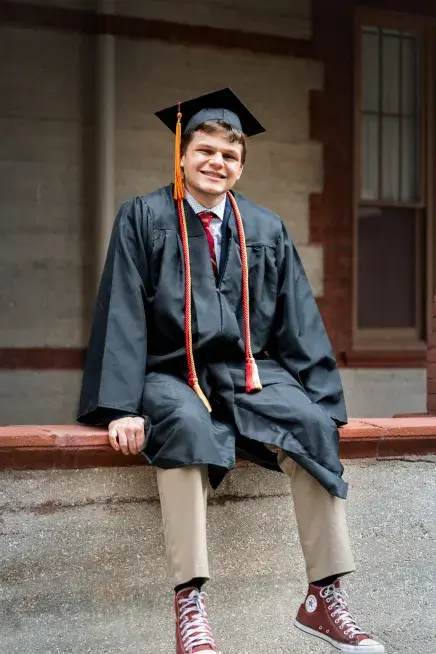 Tyler Newman sitting on a ledge outside of The Ponce in his graduation gear