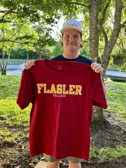 Aiden McGee holding up a Flagler tee shirt for the camera