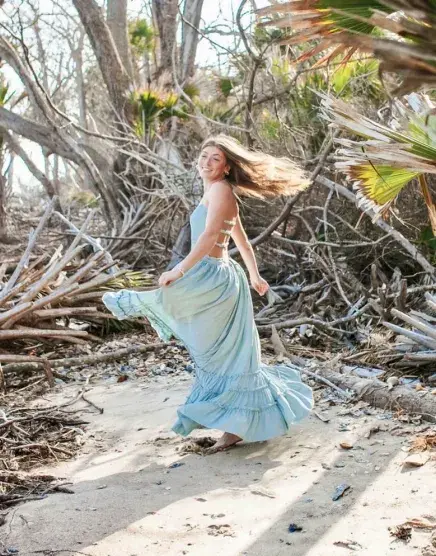 Grayson Rice stands in a wooded beach area with a blue dress on