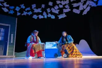 Stage shot from "Almost Maine". Two students wearing winter clothes speaking to each other.
