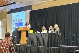 2024 Women in Sport panelists on stage with screen displaying the event name behind them.