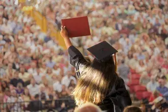 Student crossing stage at graduation, holding up diploma