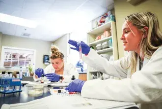 Students wearing lab coats and gloves working in the science lab