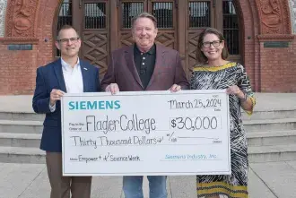 Steve Hoiberg, President Delany, and Laura Stevenson hold a large check from Siemens for $30,000