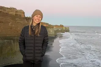Student Katie Kress poses for a photo on the New Zealand cliffside with the ocean behind her
