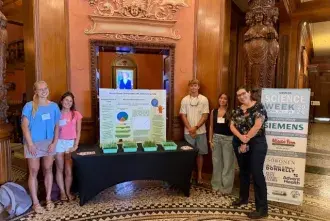 Students standing by their public research showcase table in the Ponce rotunda