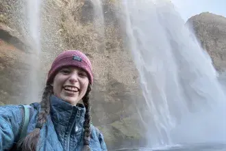 Amelie Thompson smiles for a selfie with a waterfall behind her
