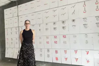 CEAM Antebi - woman wearing black top and skirt standing in front of artwork full of symbols
