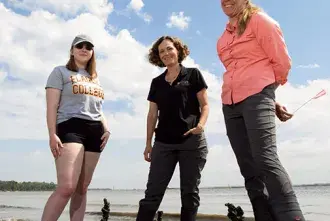 Student and professors standing around oysters on a river shore