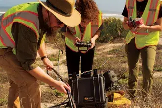 A professor and students on the beach working on their robot