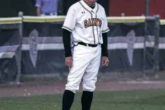 Dressed in a Flagler College Saints baseball uniform Coach Dave Barnett stands on the baseball field