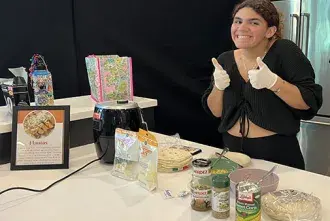 Student at LASO cooking event smiles and gives thumbs up while presenting dish