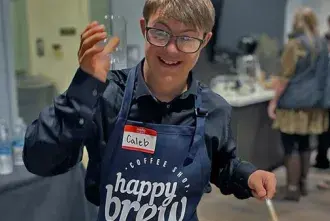 Happy Brew employee with branded apron holding up a cup