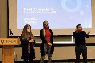 Flagler Professors June Ann LeFors and Jennifer Catalano stand in front of a project screen for a presentation.