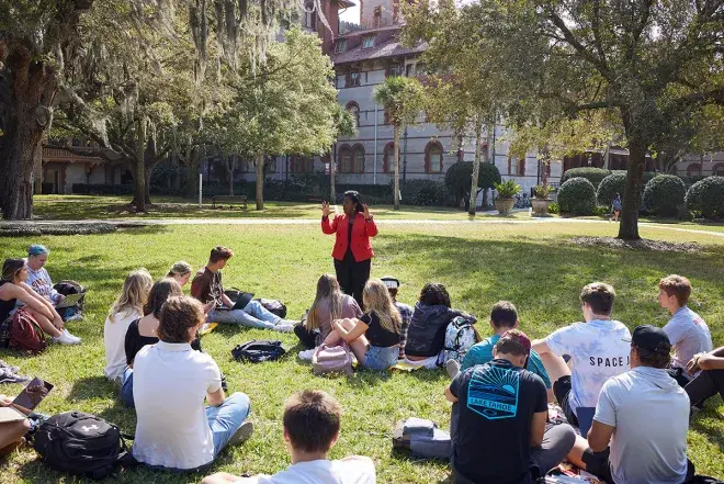 A professor teaching to their class of students who are sitting on the grass of the West Lawn