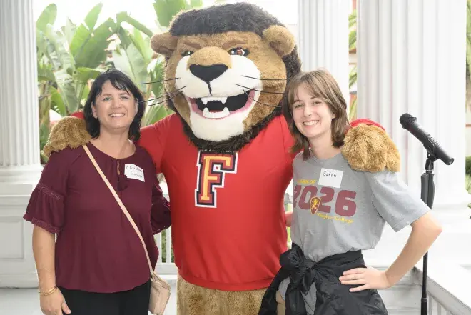 Flagler College's Lewis the Lion poses with a student and family member.