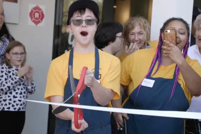 A youth cuts a ribbon to celebrate the grand opening of a new coffee shop.
