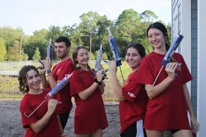 A group of students holds caulking guns for a volunteer project