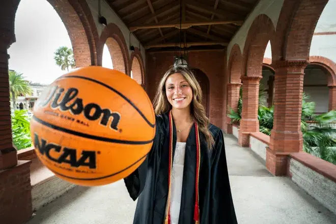 Student in cap and gown holding basketball