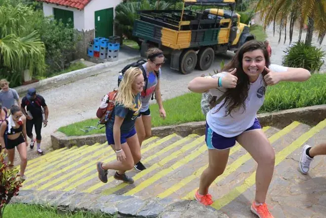  Student climb steps outdoors in rural area, and one student gives thumbs up to the camera. 