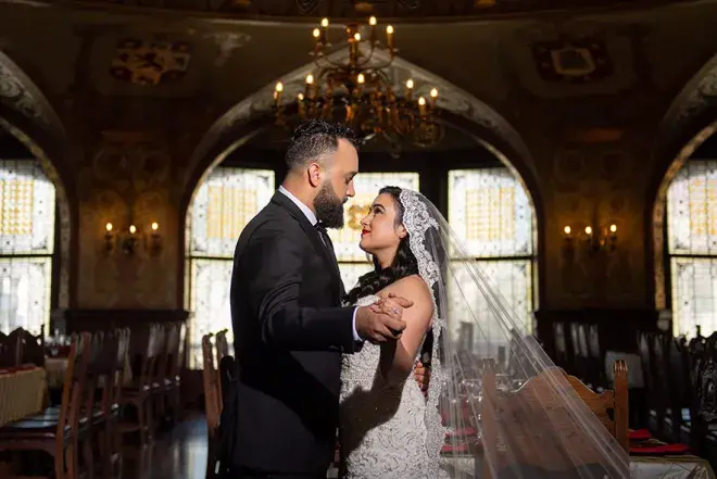 A bride and groom stand in the middle of the ballroom