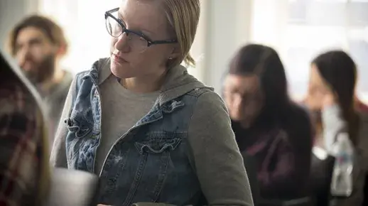 Seated student in glasses looks towards professor. 