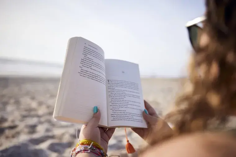 Student reading a book on the beach.