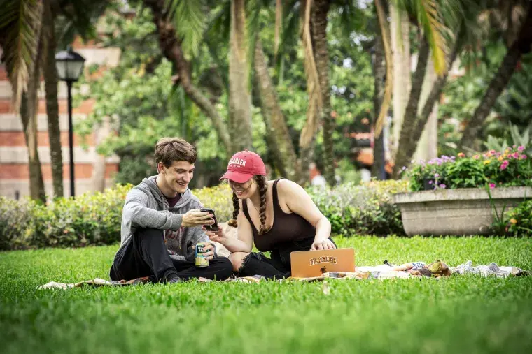 Two students sitting on a blanket on the grass of Flagler College