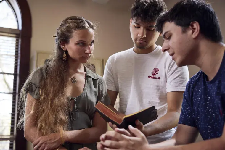 Three Flagler College students examine an old book.