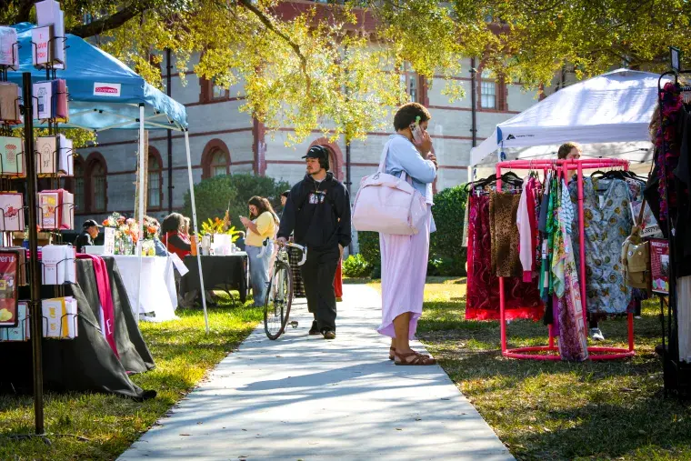 A shot down a sidewalk with Mini Mane Market booths on each side of the sidewalk. Two students stand browsing the market.