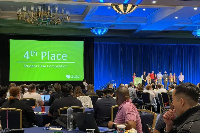 Ballroom full of people at table and students on stage accepting an award