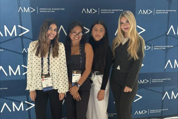 Four students pose for a photo in front of a AMA branded backdrop