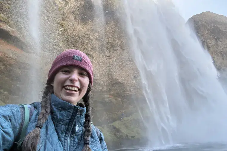 Amelie Thompson smiles for a selfie with a waterfall behind her