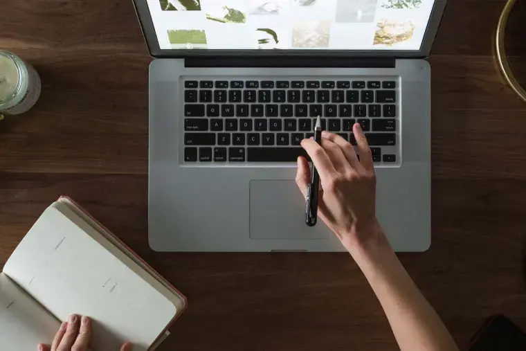 A young woman typing on a computer while taking notes 