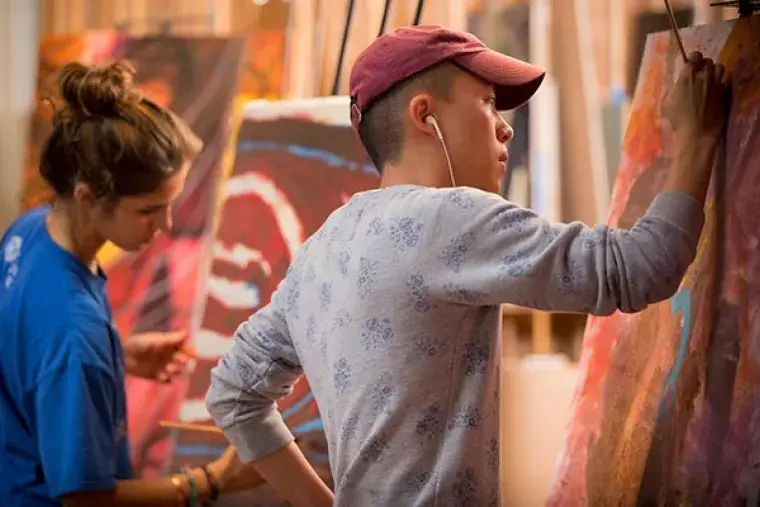 Male student and female student paint on large canvases. 