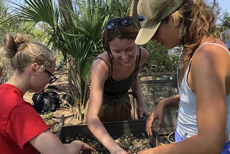 Three students sifting through dirt at Fort Mose.