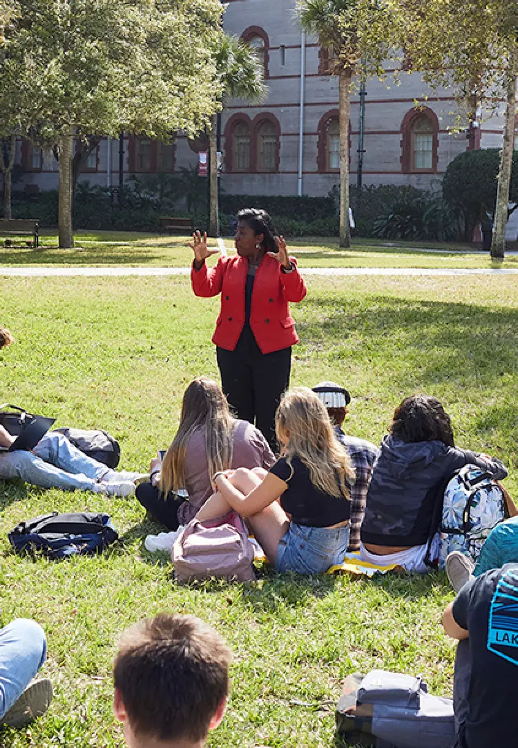 A professor teaching to their class of students who are sitting on the grass of the West Lawn
